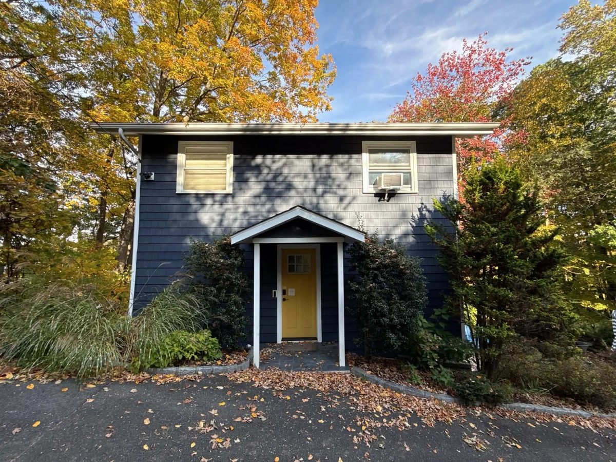 Original phone photo of a navy house with a yellow door, patchy shade on the siding under a pale sky